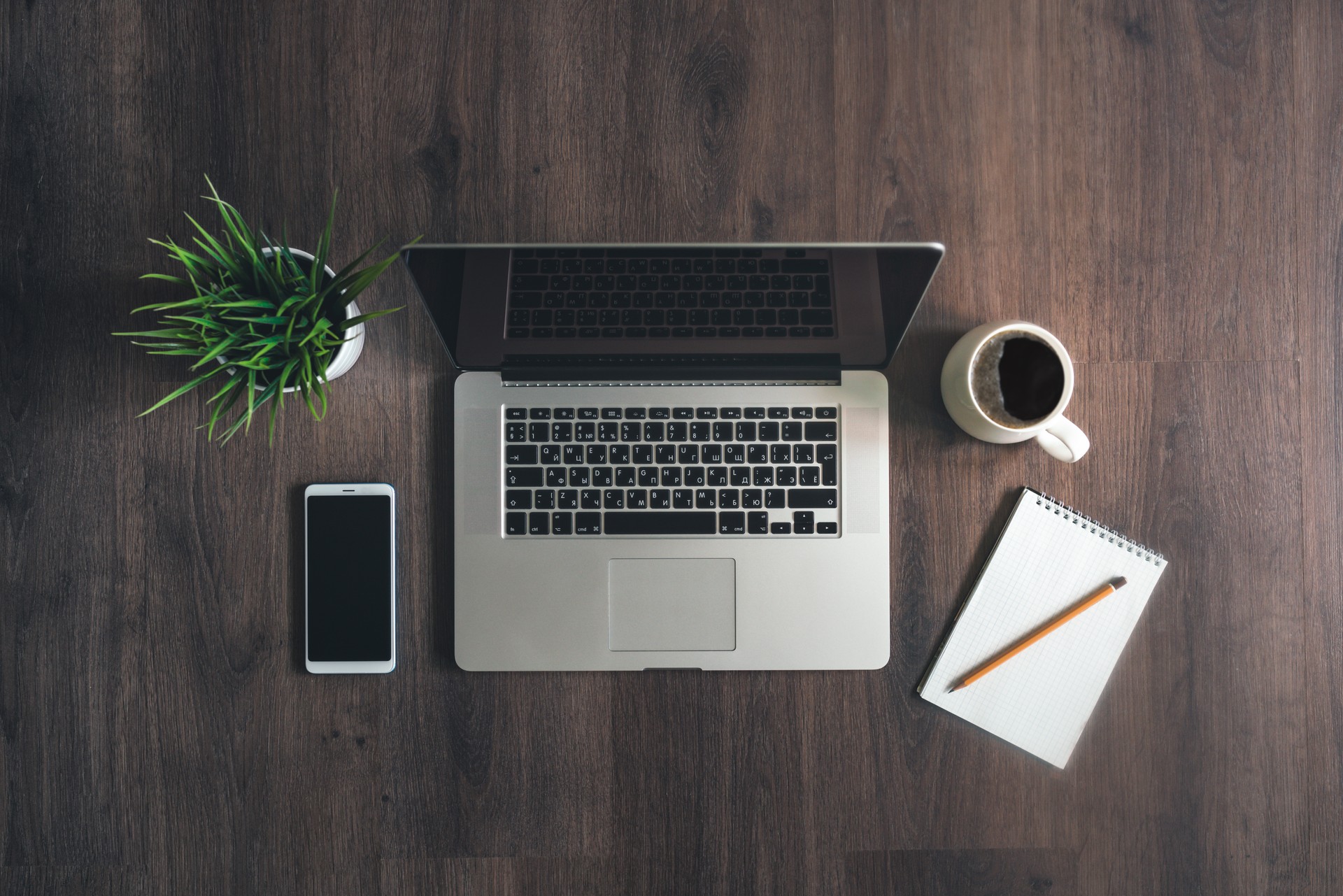 Laptop, smartphone, note book, pencil and cup of coffee on a wooden table